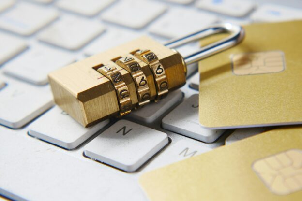 A golden combination padlock sitting on a computer keyboard by some credit cards.